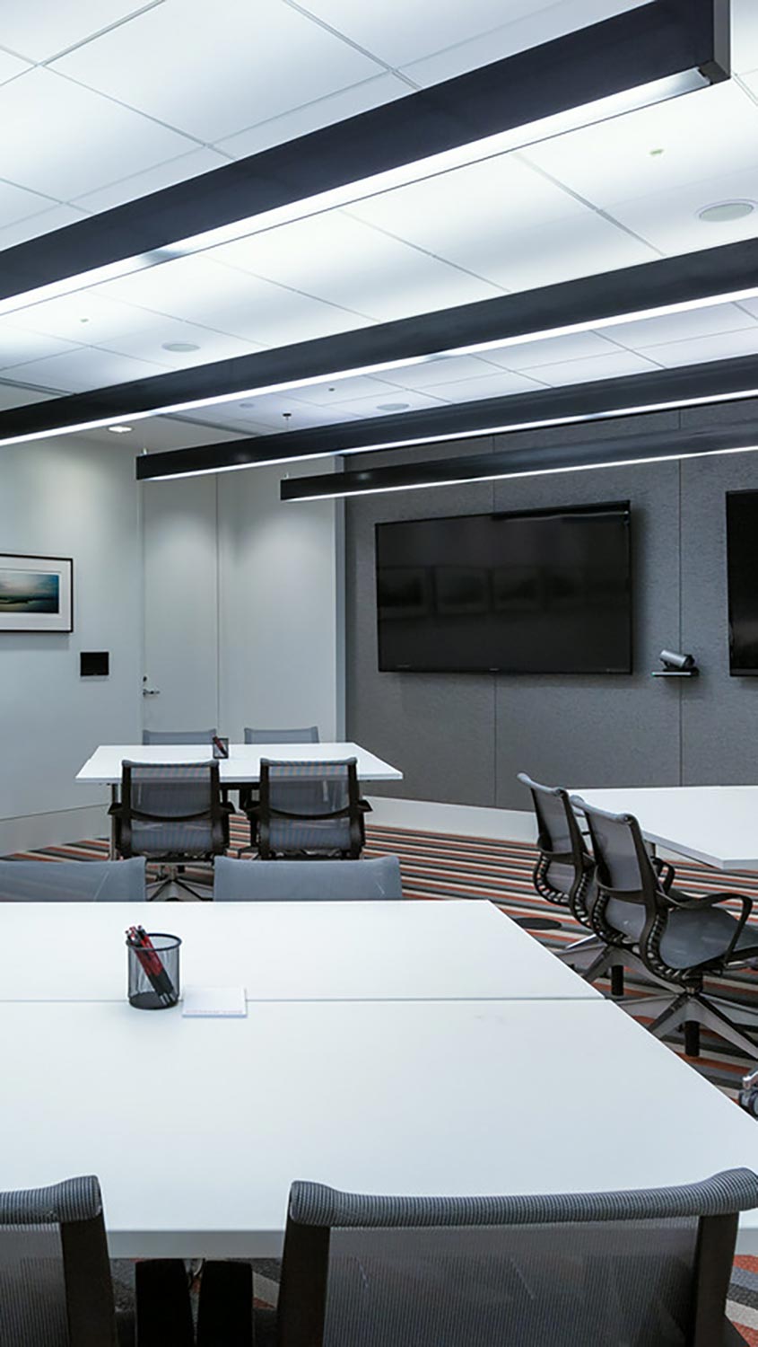 Contemporary conference room with modular white tables, mesh office chairs, and dual wall-mounted screens