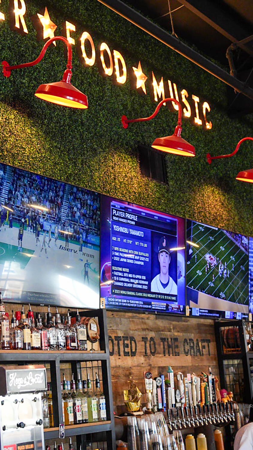 Sports bar with beer taps, wood wall backdrop, and overhead TVs broadcasting games and sports news