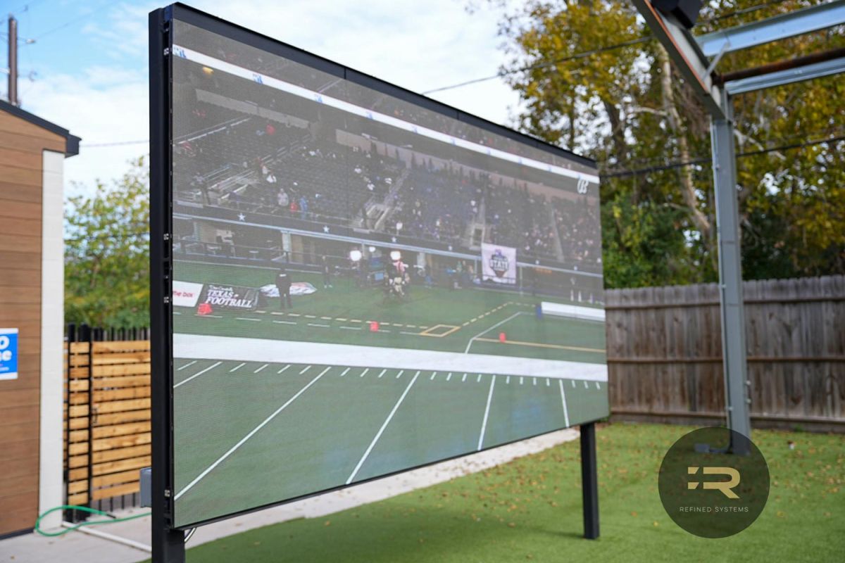 Outdoor LED screen displaying a football game over synthetic turf.