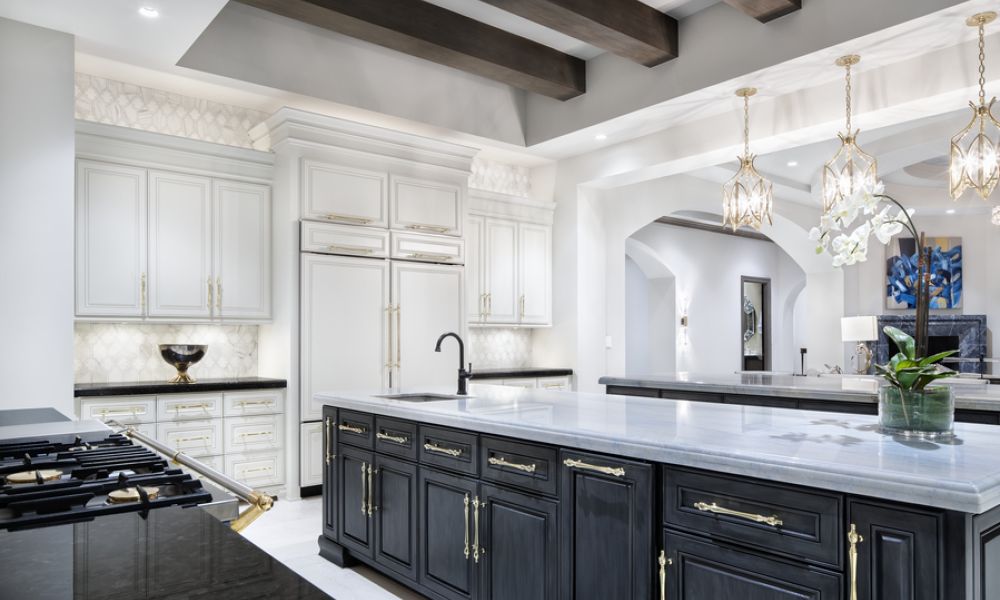 <span class="uk-h4">A luxurious modern kitchen with a large island, elegant lighting fixtures, white cabinetry, and gold accents.</span>