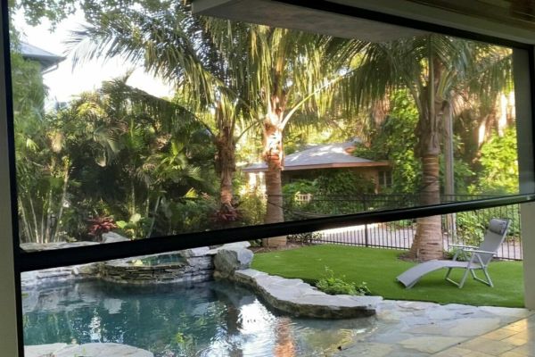 patio screen partially lowered over a pool and palm tree backyard with stone patio and lounge chair