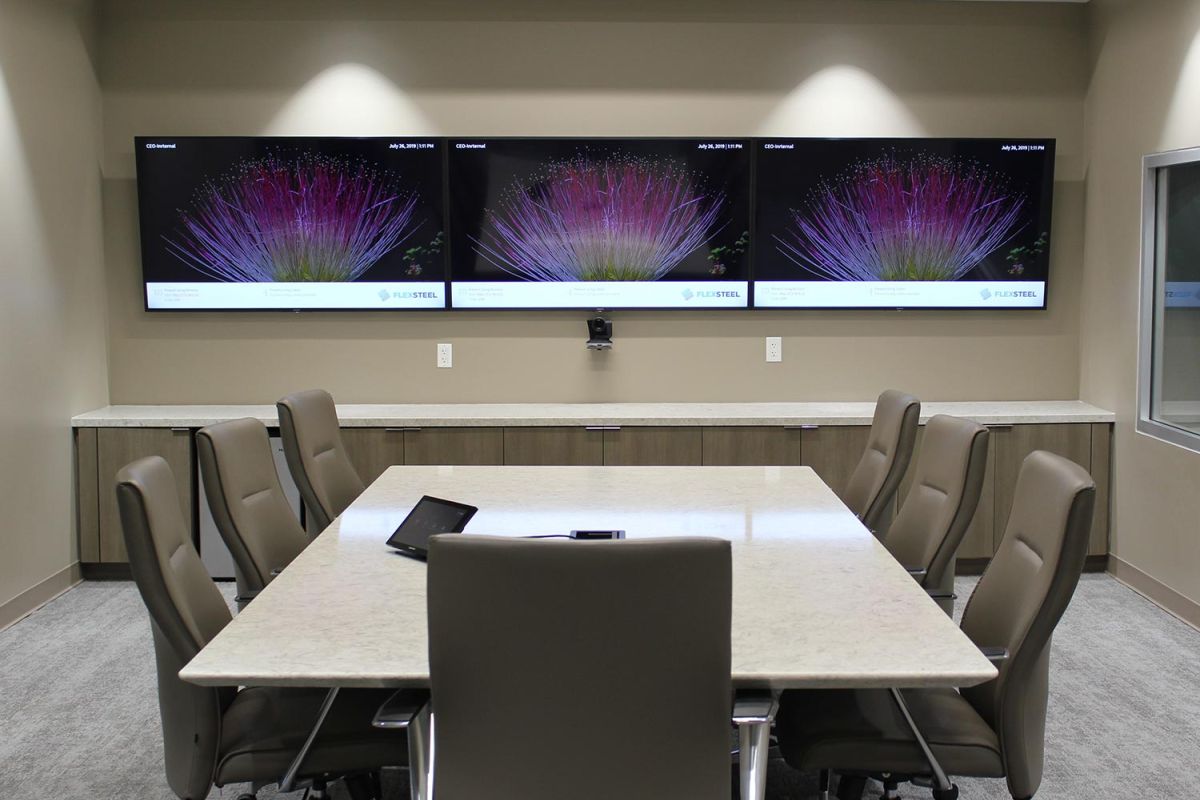Boardroom with triple displays showing digital art and padded chairs