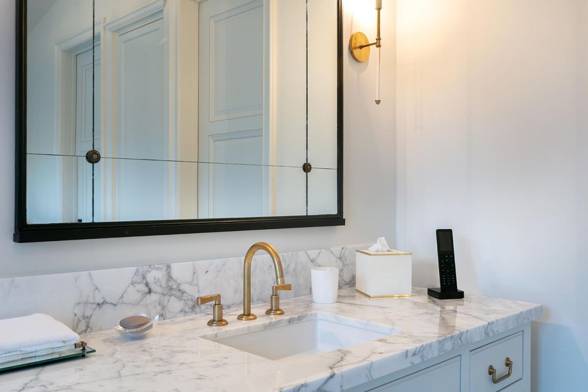 Marble bathroom countertop with gold faucet, mirror, and wall sconce lighting