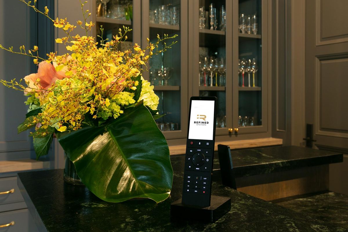 Black smart remote with Refined Systems logo on a dark stone countertop