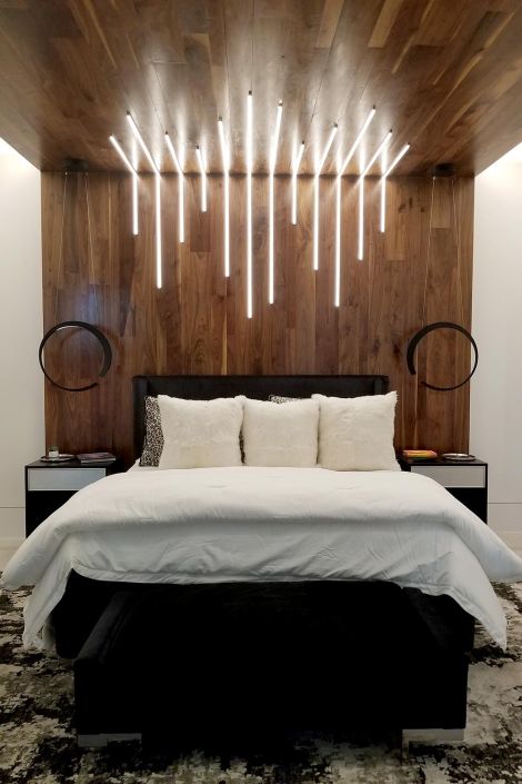 Modern bedroom with wood-paneled accent wall and ceiling, featuring vertical pendant lights above a bed with white pillows and bedding