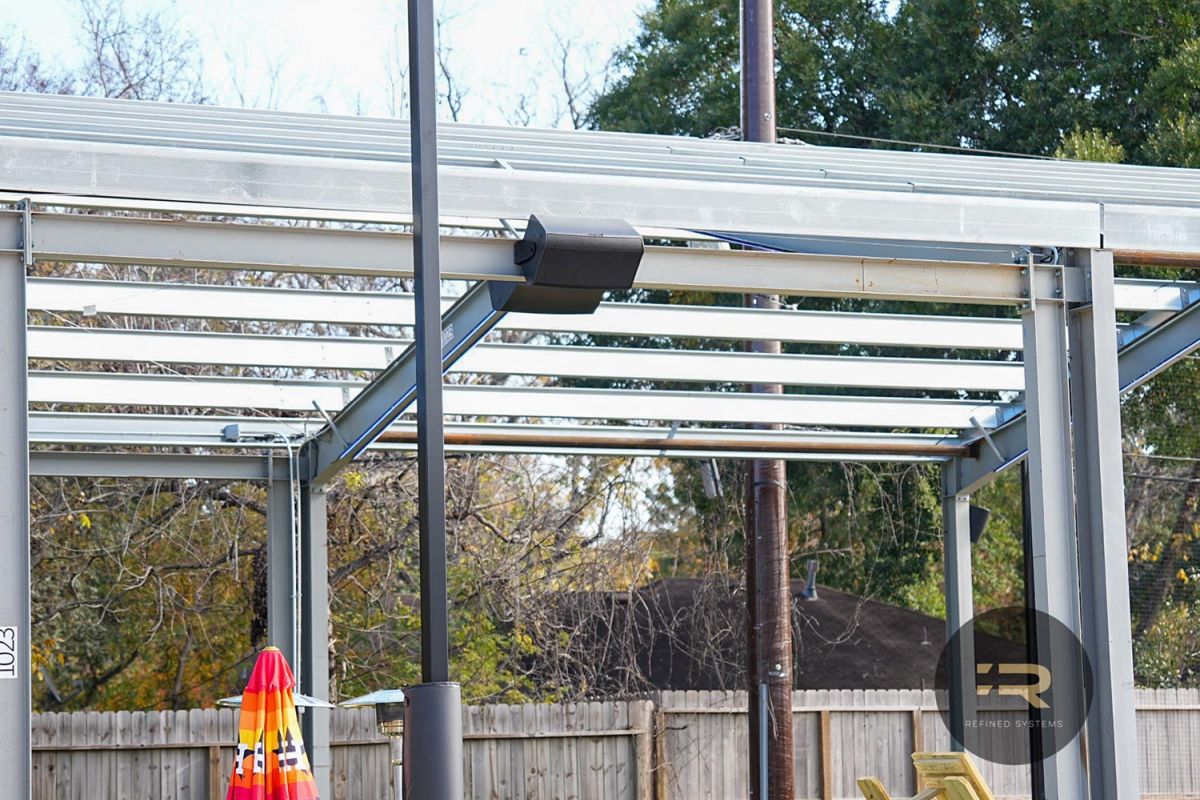 Black speaker mounted on a metal frame in a covered outdoor space.