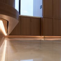 Warm LED toe-kick lighting under walnut cabinetry reflects on a polished marble floor in a luxury interior.