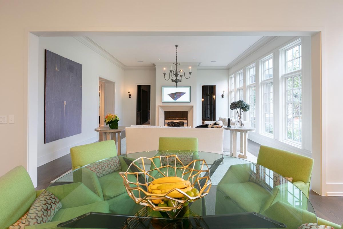 Bright dining area with green chairs, glass table, and fruit bowl centerpiece